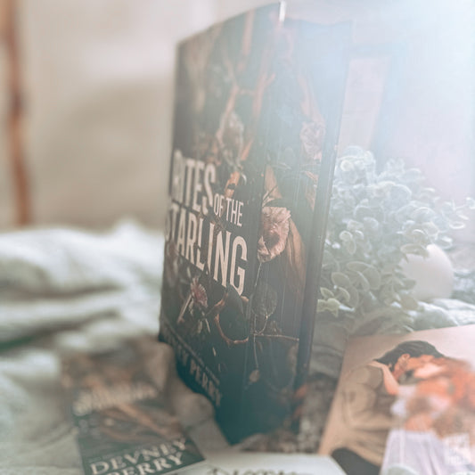 Book titled 'Rites of the Starling' by Devney Perry on a textured surface with a plant and other books.