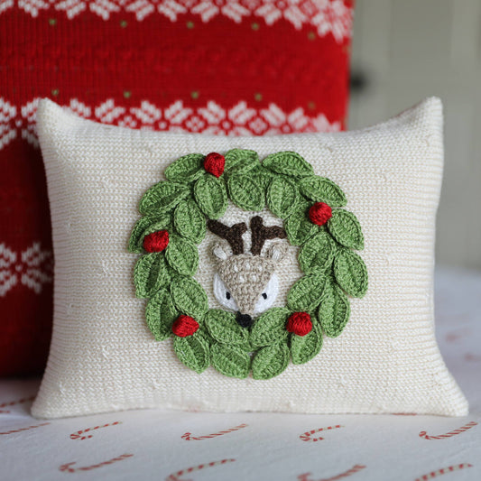 Decorative pillow with a crochet deer in a wreath design on a white background