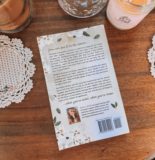 Book titled 'You Can Feel It in the Silence' by Emily A. Myers on a wooden surface with a glass of orange juice and a candle.