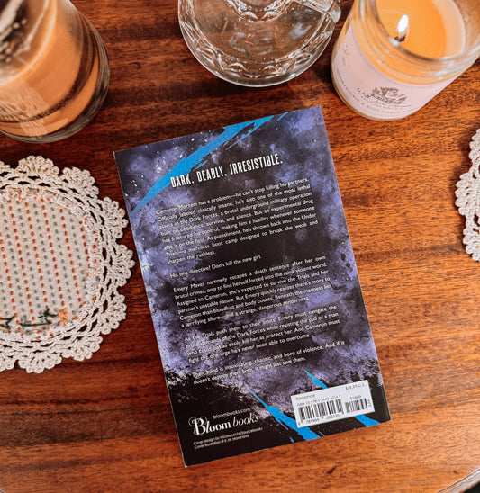 Book titled 'Your Knife My Heart' by K.M. Moronova on a wooden surface with candles and doilies.