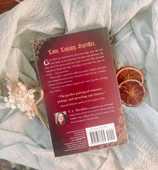 Book titled 'The Second Death of Locke' by L. Bovalino on a textured fabric background with dried oranges and flowers.