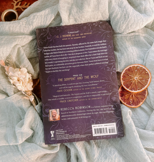 Book titled 'The Serpent and the Wolf' by Rebecca Robinson on a textured surface with decorative elements.