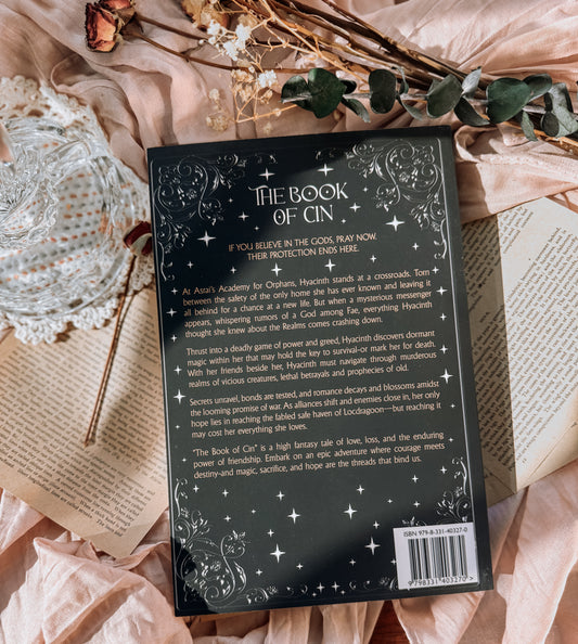 Book titled 'The Book of Cin' by H.M. Wolfe on a decorative surface with flowers and lace.