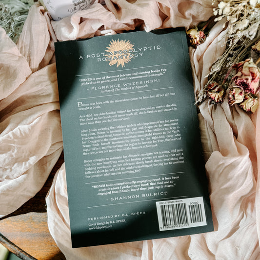 Book titled 'Bones' by K.L. Speer on a soft fabric background with flowers.