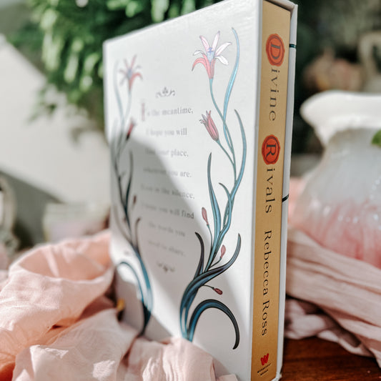 Book titled 'Divine Rivals' by Rebecca Ross with floral design on a soft fabric background