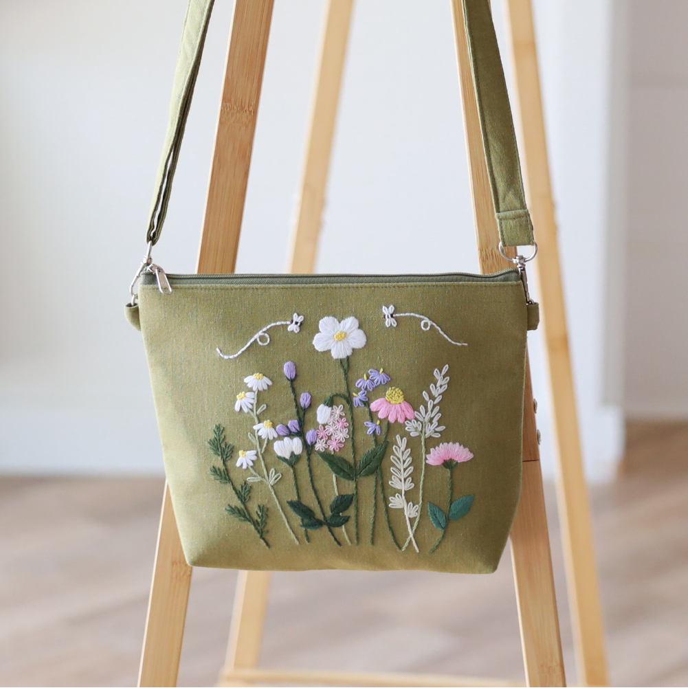 Green handbag with floral embroidery on a wooden stand indoors.