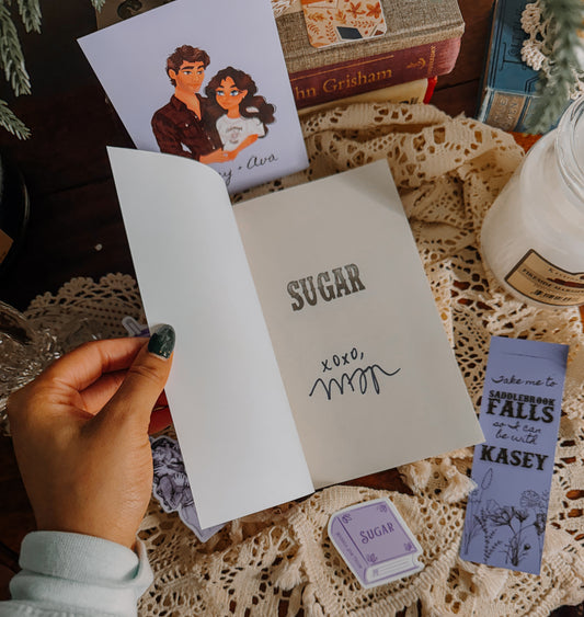 Book titled 'Sugar' by Michaela Jean Taylor with related merchandise on a lace tablecloth.