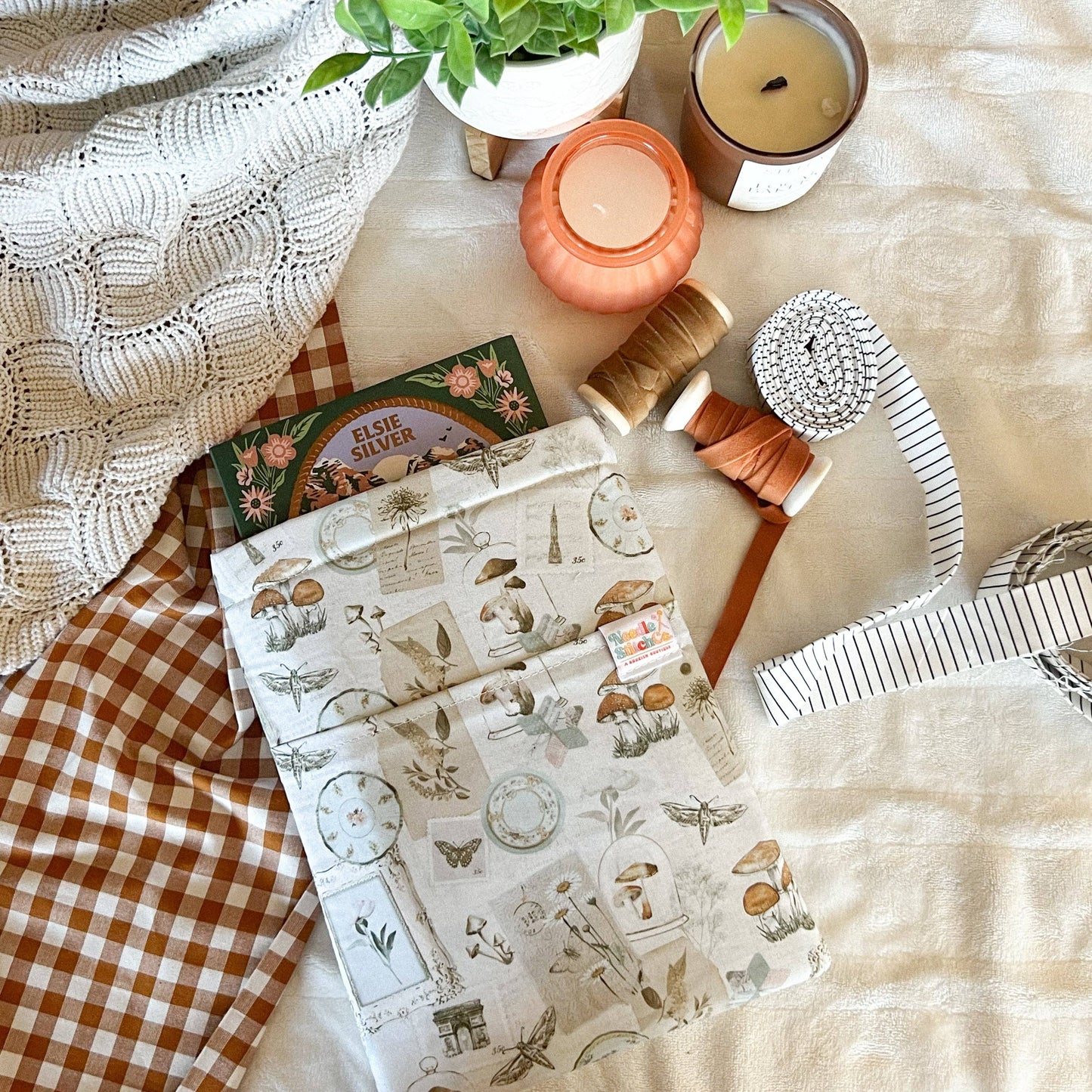 Flat lay of stationery items including a notebook, candles, and a plant on a textured surface. Book sleeve