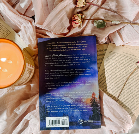 Book titled 'Bluebird Gold' by Devney Perry with a candle and flowers on a soft fabric background