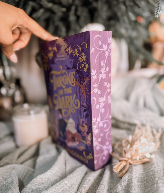 Book titled 'Throne in the Dark' by A.K. Caggiano on a textured surface with a candle and decorative elements.