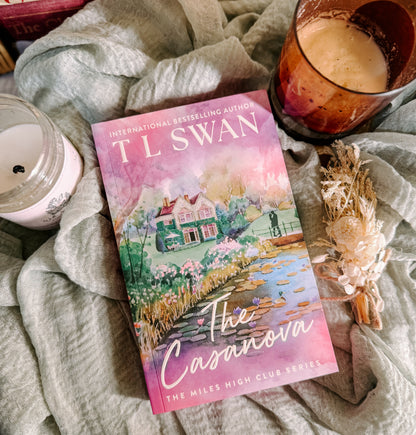 Book titled 'The Casanova' by TL Swan on a soft surface with candles and flowers.