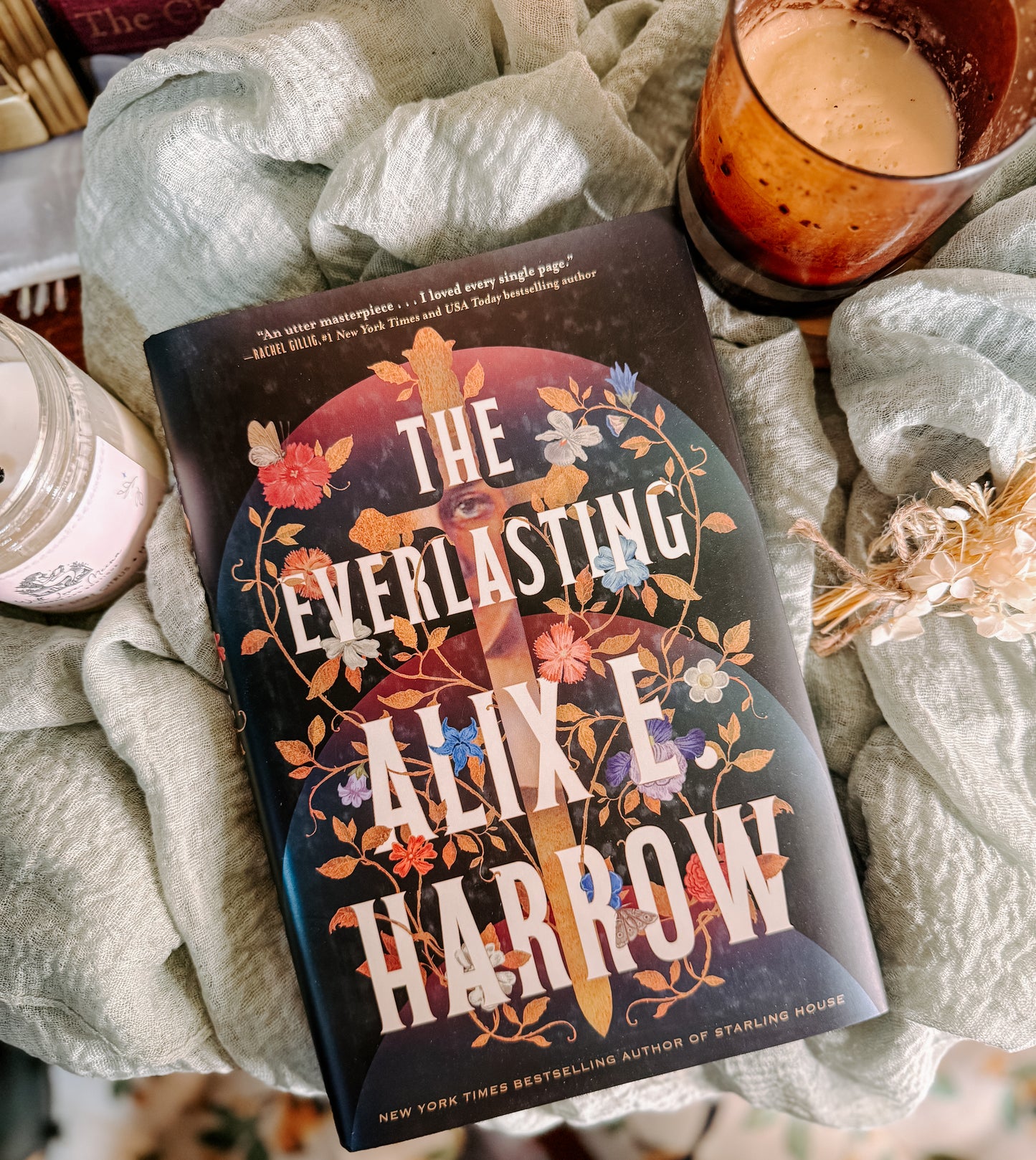 Book titled 'The Everlasting' by Alix E. Harrow on a soft surface with a candle in the background