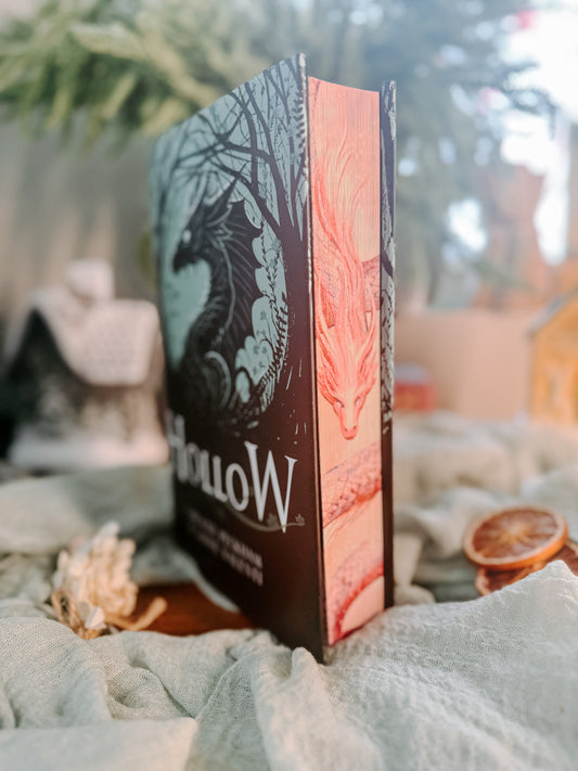 Book titled 'Hollow' by Caroline Peckham and Susanne Valenti on a soft fabric background with dried oranges.