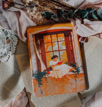 Decorative kindle case with an illustration of a woman reading by a window, surrounded by flowers and lace.