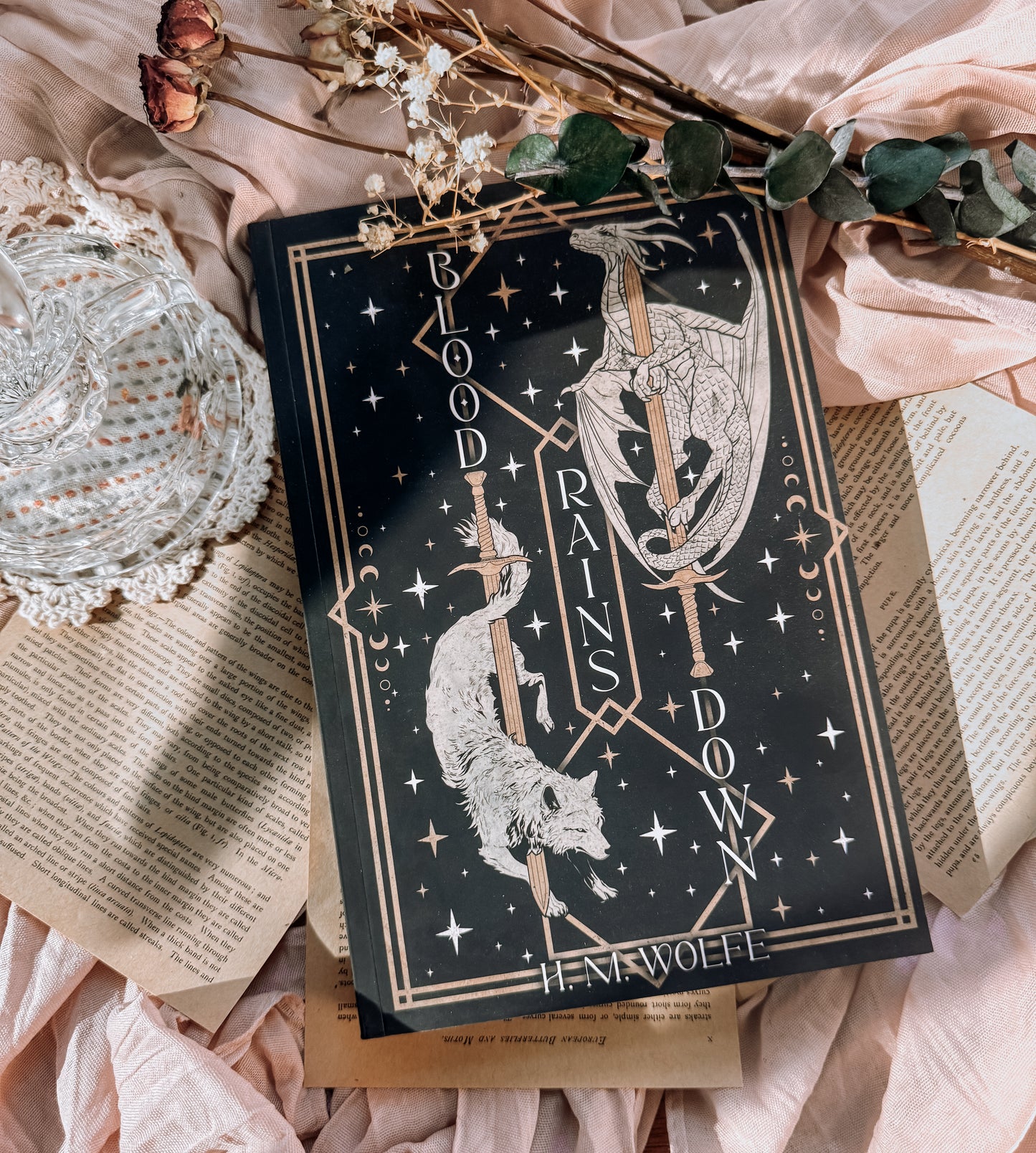 Book titled 'Blood Rains Down' with decorative elements on a soft fabric background