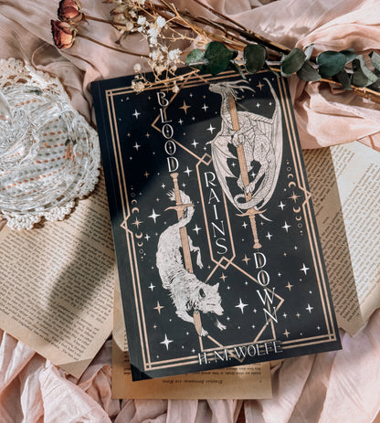 Book titled 'Blood Rains Down' with decorative elements on a soft fabric background