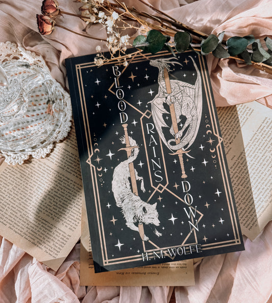 Book titled 'Blood Rains Down' with decorative elements on a soft fabric background