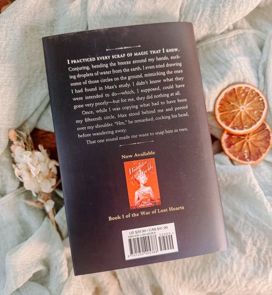 Book titled 'Children of Fallen Gods' by Carissa Broadbent on a textured surface with dried oranges.