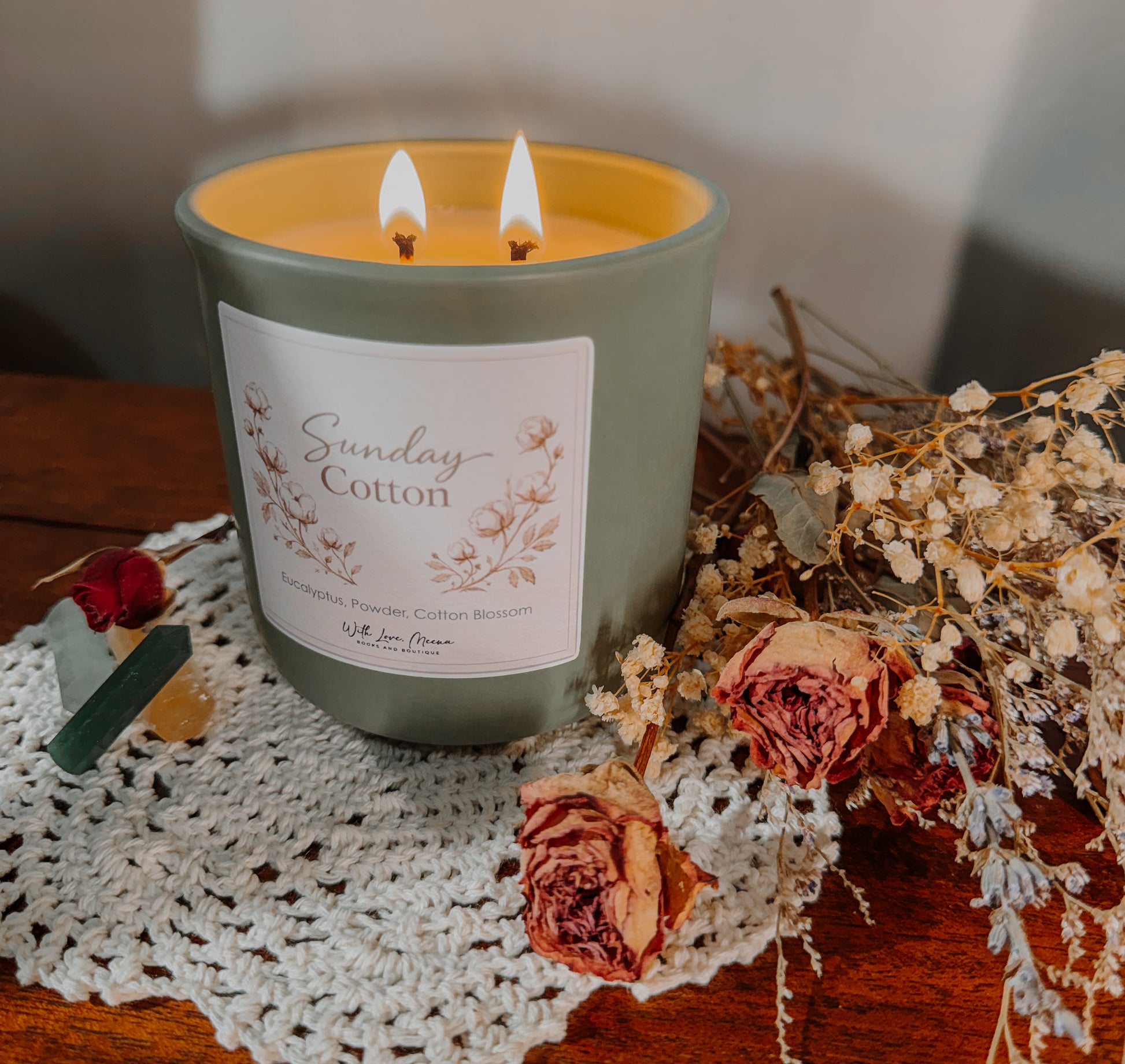 Candle labeled 'Sunday Cotton' with floral design on a doily with dried flowers.