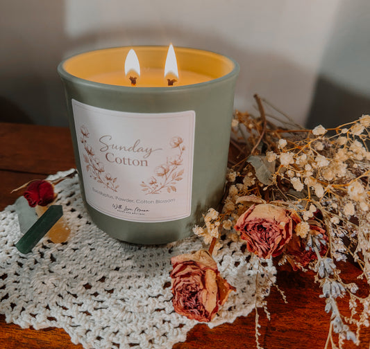 Candle labeled 'Sunday Cotton' with floral design on a doily with dried flowers.
