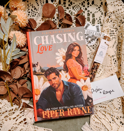 Book titled 'Chasing Love' by Piper Rayne on a decorative surface with flowers and cards.