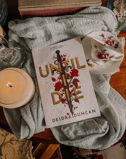 Book titled 'Until I Die' by Deidra Duncan on a textured surface with a candle and fabric.