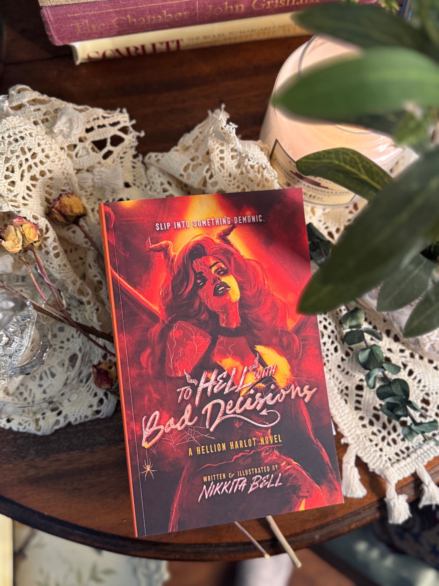 Book titled 'Hellish Bad Deliveries' on a lace tablecloth with a plant in the background