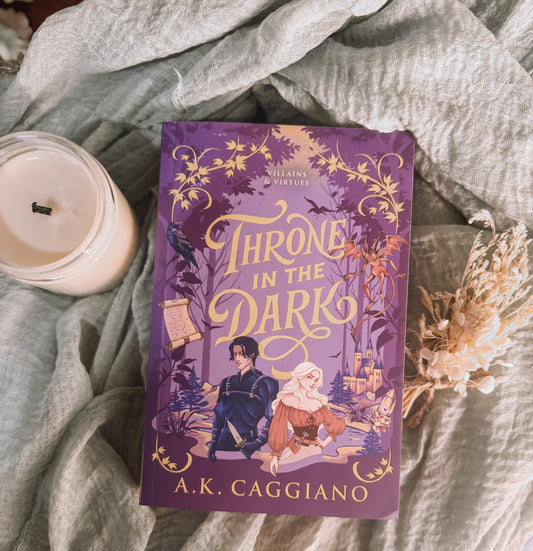 Book titled 'Throne in the Dark' by A.K. Caggiano on a textured surface with a candle and decorative elements.