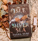 Book titled 'The Isle of Silver Sea' by Tasha Suri on a decorative background with flowers and lace.