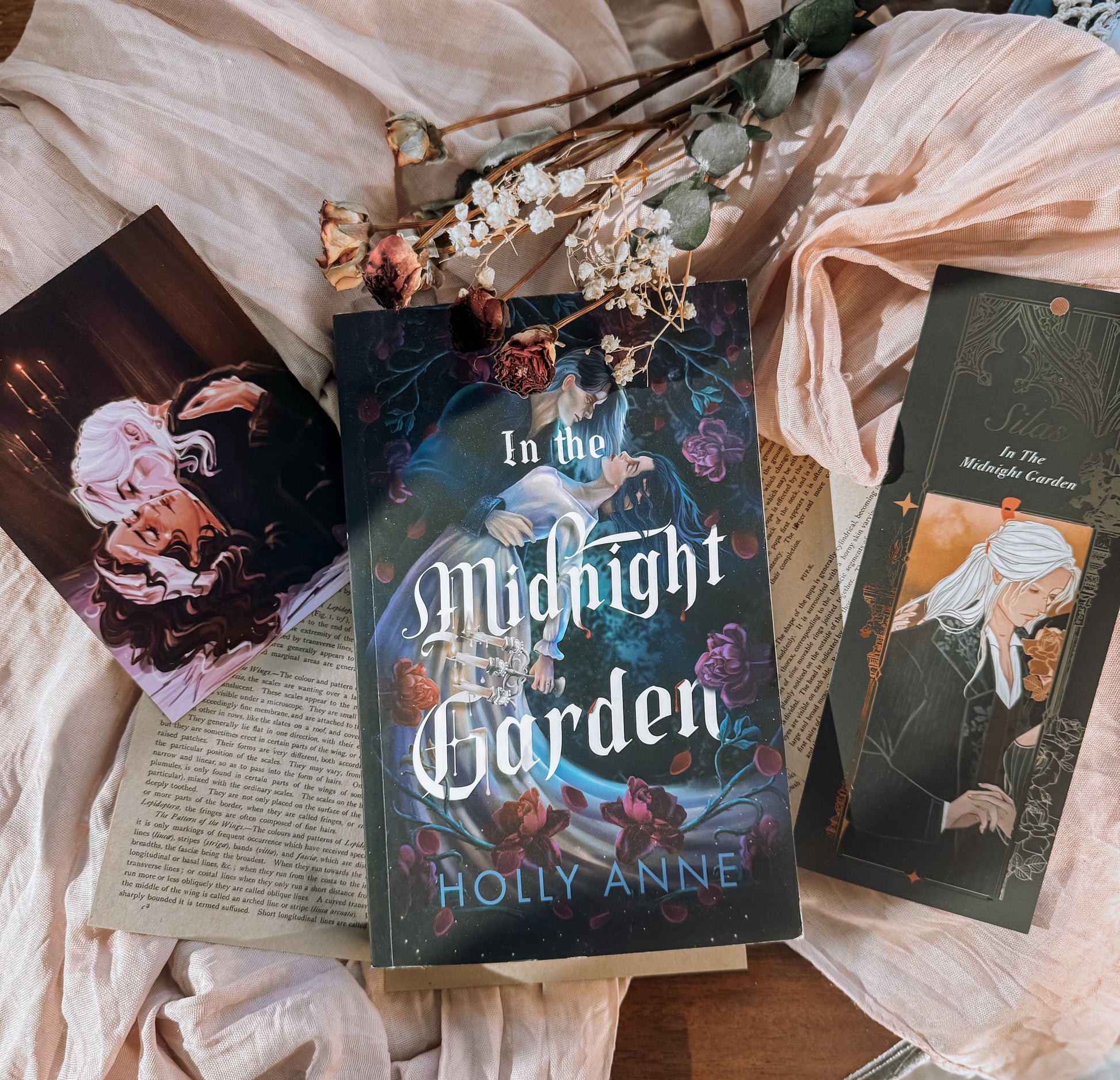 Book titled 'In the Midnight Garden' by Holly Anne on a bed with floral decorations.