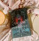 Book titled 'Arcane Inheritance' by Kamilah Cole on a soft fabric background with a candle and flowers.