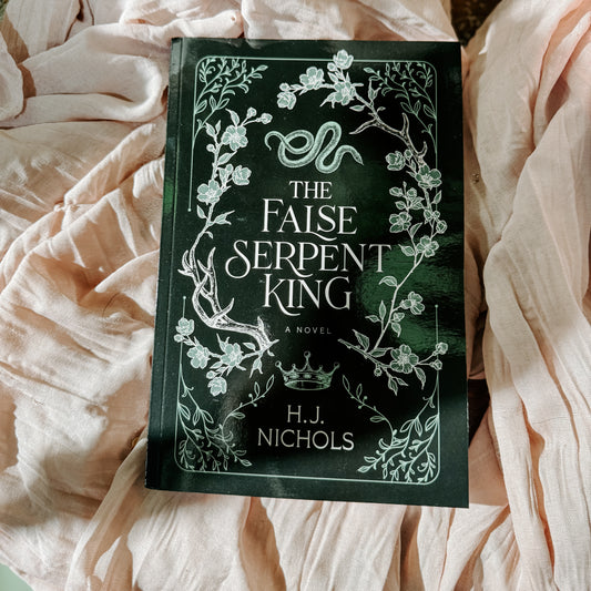 Book titled 'The False Serpent King' by H.J. Nichols on a soft fabric background