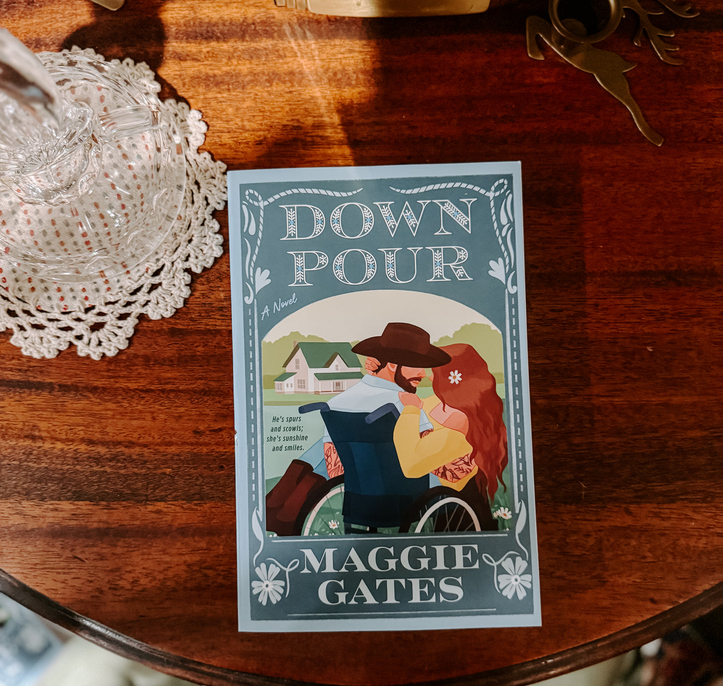 Book cover of 'Down Pour' by Maggie Gates on a wooden surface with decorative items.