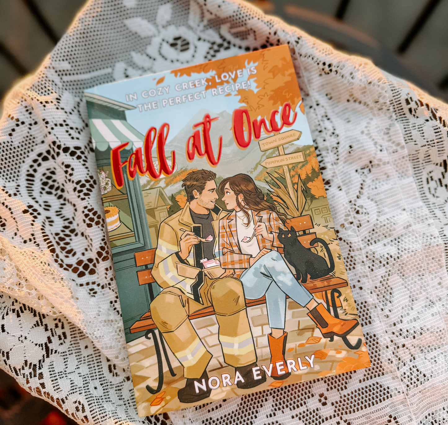 Book titled 'Fall at Once' by Nora Everly on a lace tablecloth