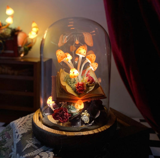 Decorative setup with mushrooms, flowers, and a book under a glass dome on a checkered floor.
