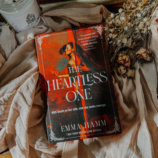 Book titled 'The Heartless One' by Emma Hamm on a textured surface with dried flowers.