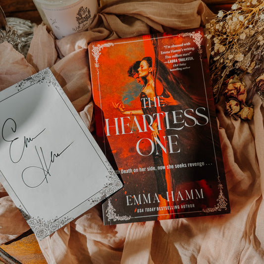 Book titled 'The Heartless One' by Emma Hamm on a textured surface with dried flowers.