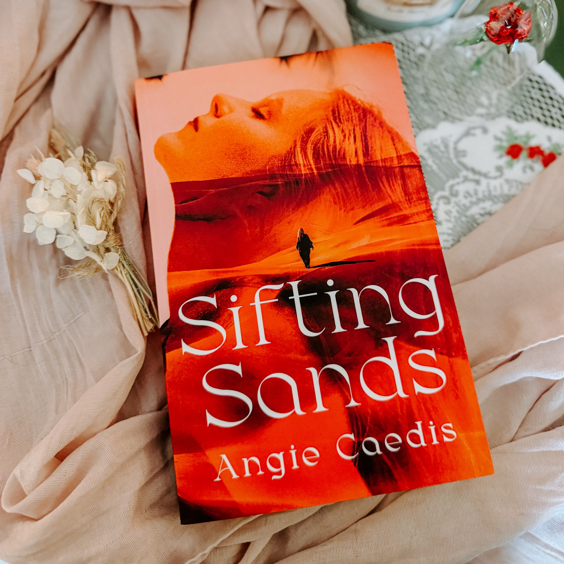 Book titled 'Sifting Sands' by Angie Caedis on a soft fabric background