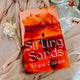 Book titled 'Sifting Sands' by Angie Caedis on a soft fabric background