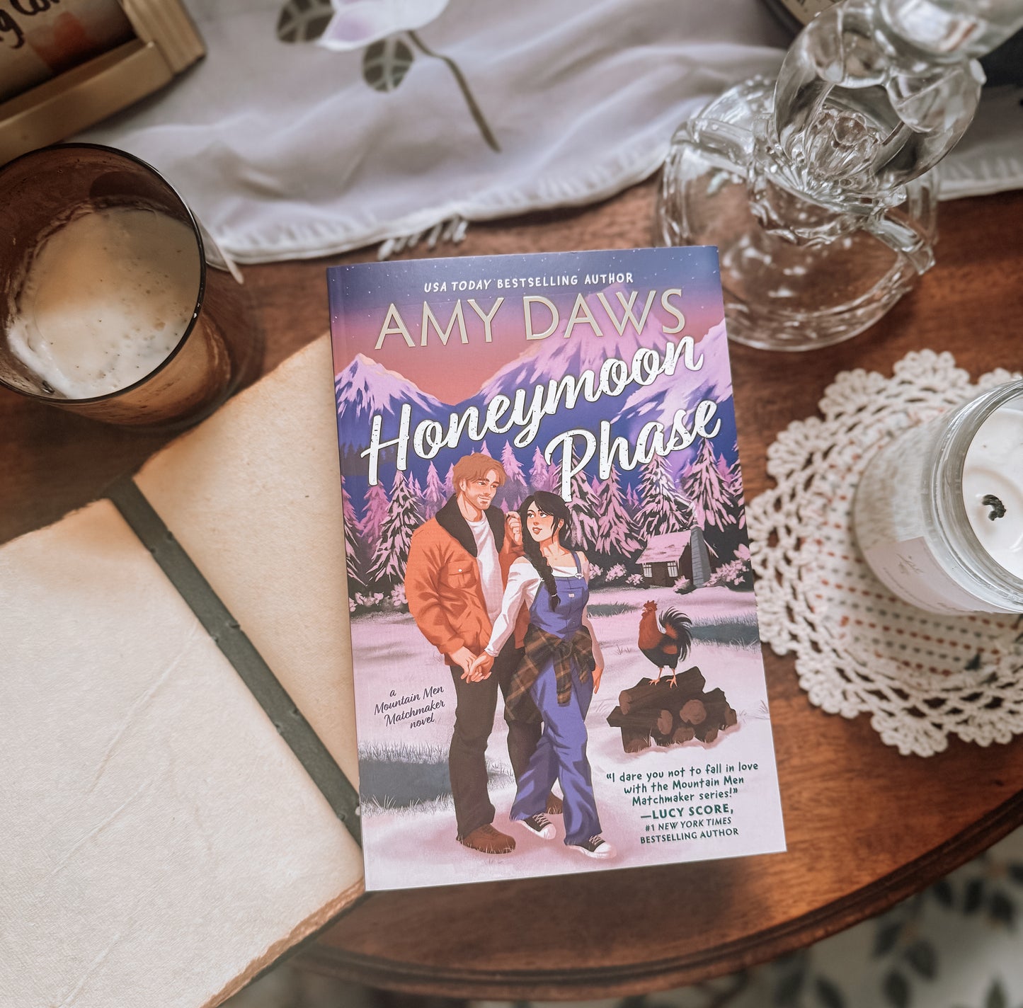 Book titled 'Honeymoon Phase' by Amy Daws on a wooden table with a glass of a frothy beverage.
