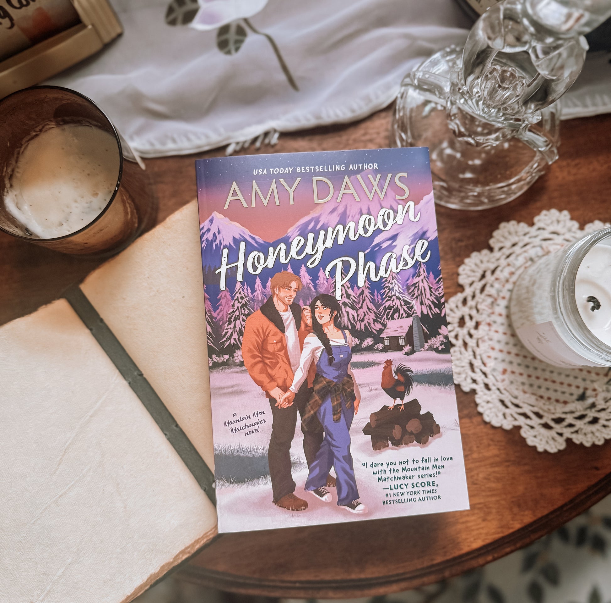Book titled 'Honeymoon Phase' by Amy Daws on a wooden table with a glass of a frothy beverage.