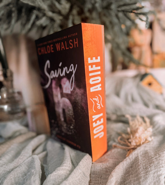 Book titled 'Saving 6' by Chloe Walsh on a textured surface with a candle and decorative elements.