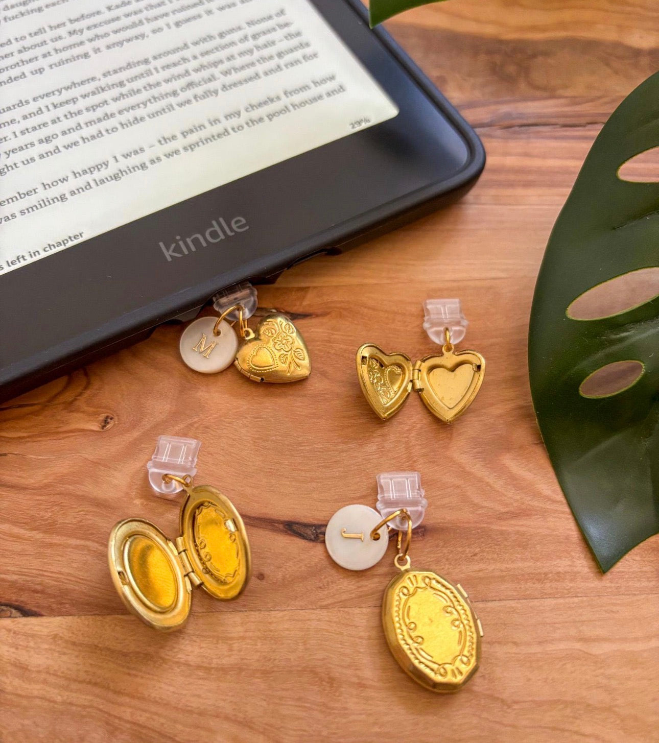 Gold heart-shaped earrings with clear clips on a wooden surface next to a Kindle device. Kindle dust plug 