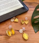 Gold heart-shaped earrings with clear clips on a wooden surface next to a Kindle device. Kindle dust plug 