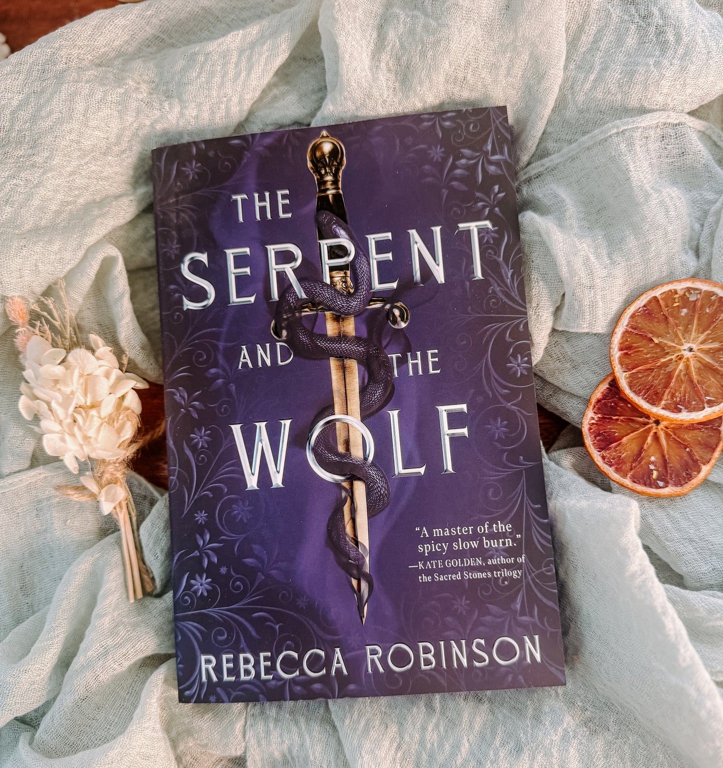 Book titled 'The Serpent and the Wolf' by Rebecca Robinson on a textured surface with decorative elements.
