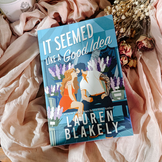 Book titled 'It Seemed Like a Good Idea' by Lauren Blakely on a soft fabric background with flowers.