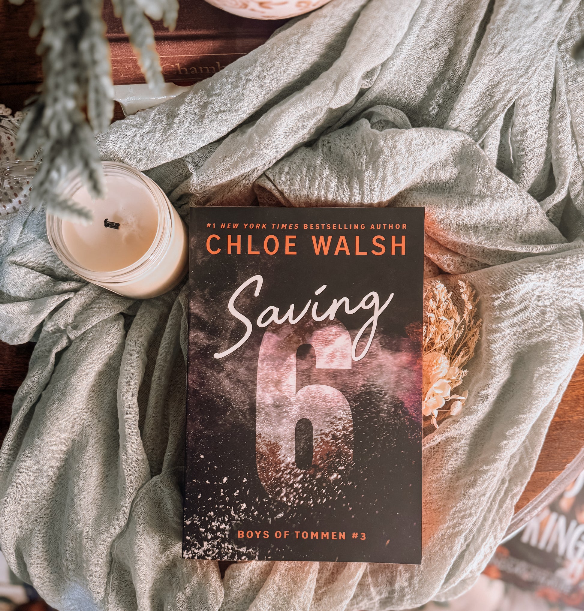 Book titled 'Saving 6' by Chloe Walsh on a textured surface with a candle and decorative elements.
