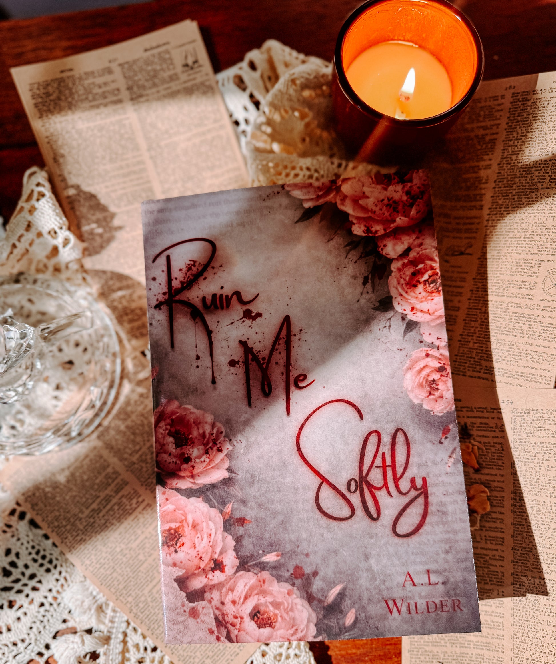 Book titled 'Ruin Me Softly' by A.L. Wilder on a table with a candle and flowers.