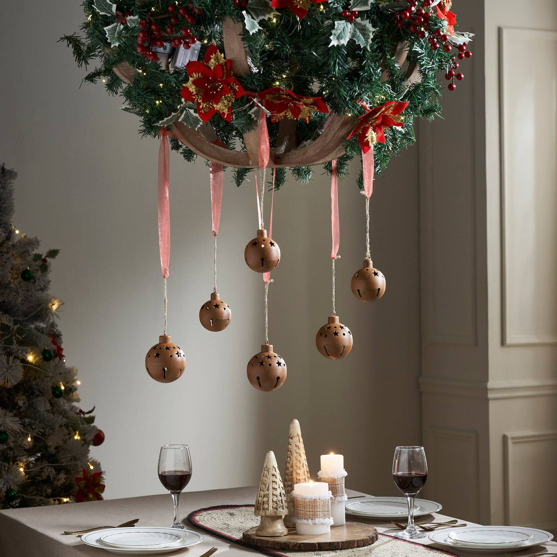 Decorative Christmas wreath with ornaments hanging over a table set for dinner.