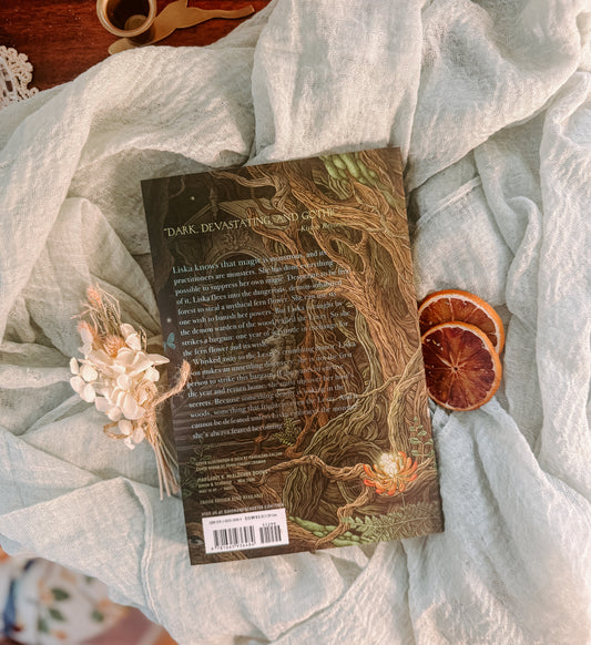 Book titled 'Where the Dark Stands Still' by A.B. Poranek on a soft fabric background with dried oranges and flowers.